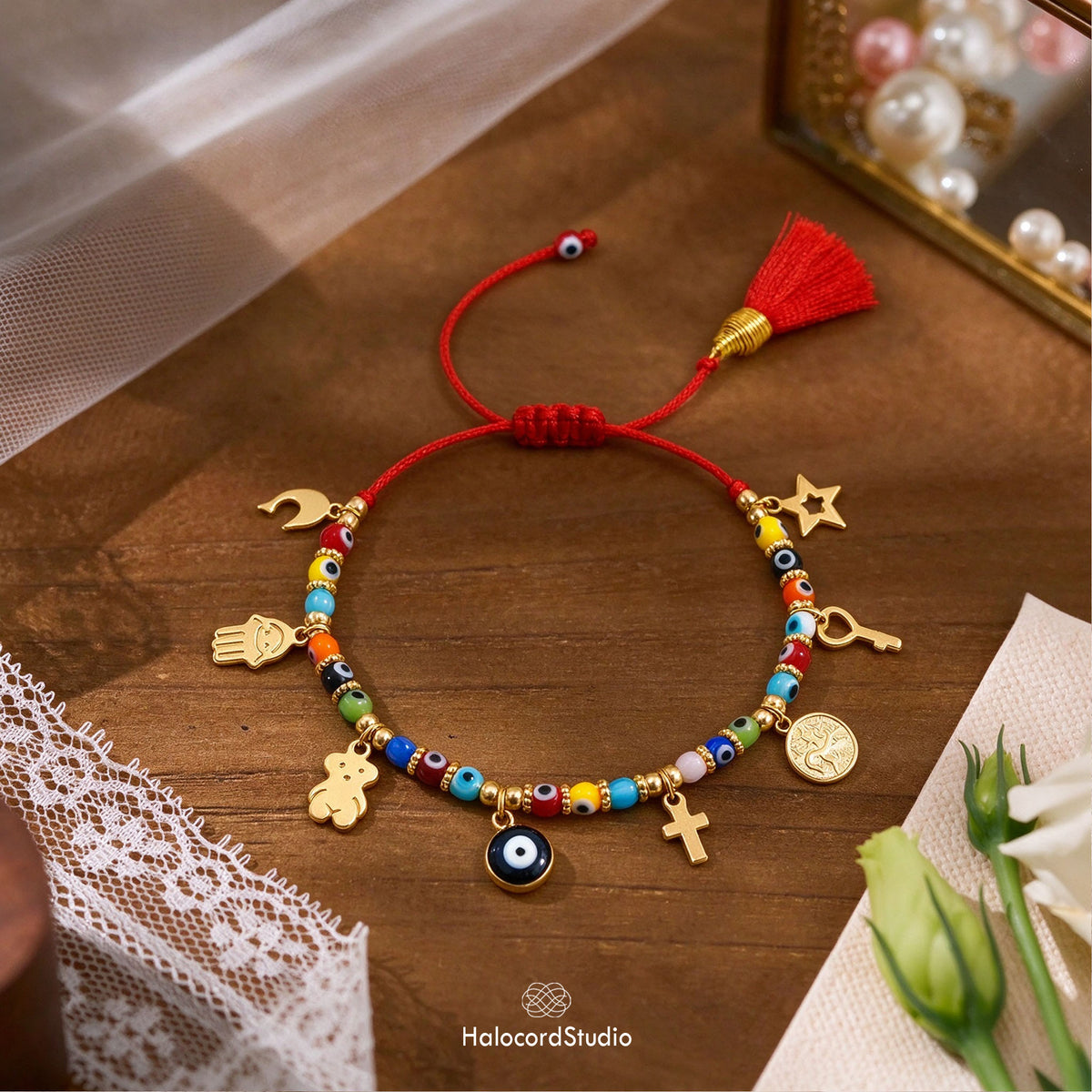 Close-up of artisan red string evil eye bracelet showing 8 golden charms including Hamsa, cross, and key on rustic wood