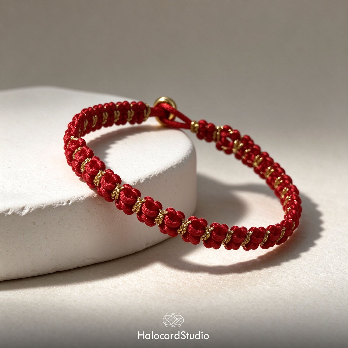 Detailed view of the handcrafted red and gold bowknot braid pattern and gold clasp bead on a white display pedestal