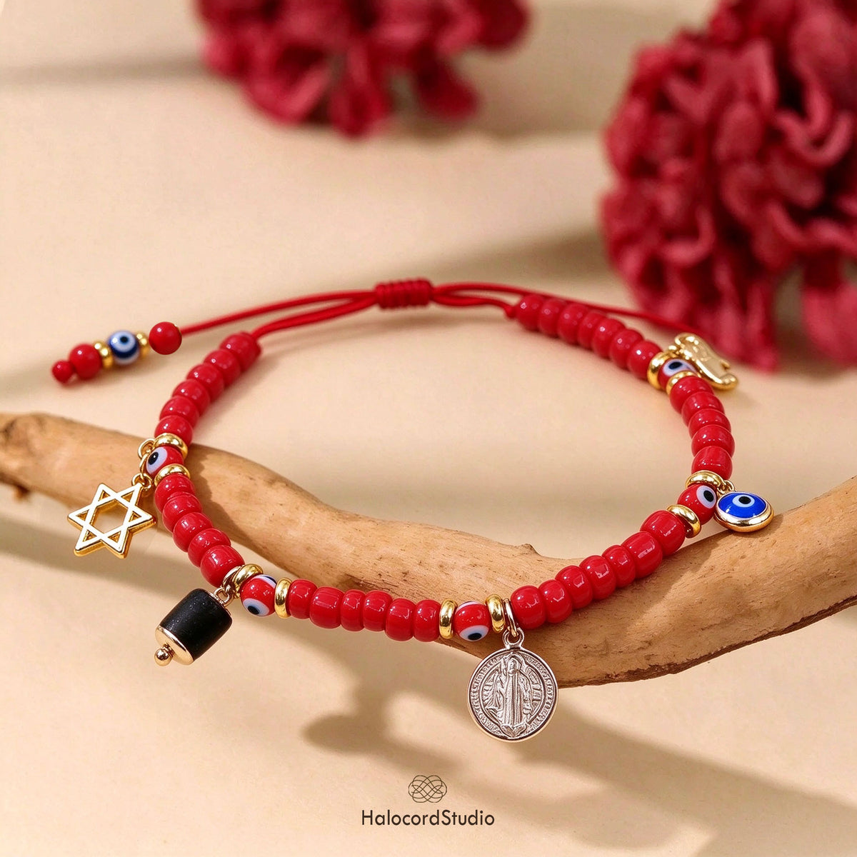 Red beaded evil eye amulet bracelet with 5 charms displayed on natural driftwood