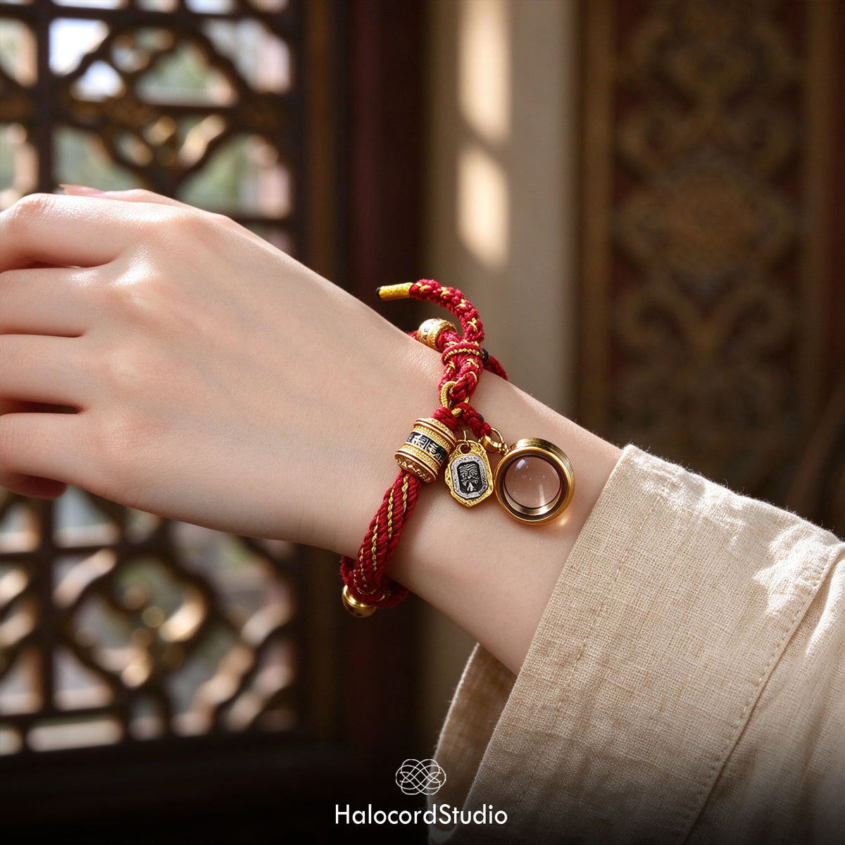 Red handwoven Tibetan lucky knot bracelet with a brass gau amulet box pendant, worn on a wrist beside a carved wooden lattice window