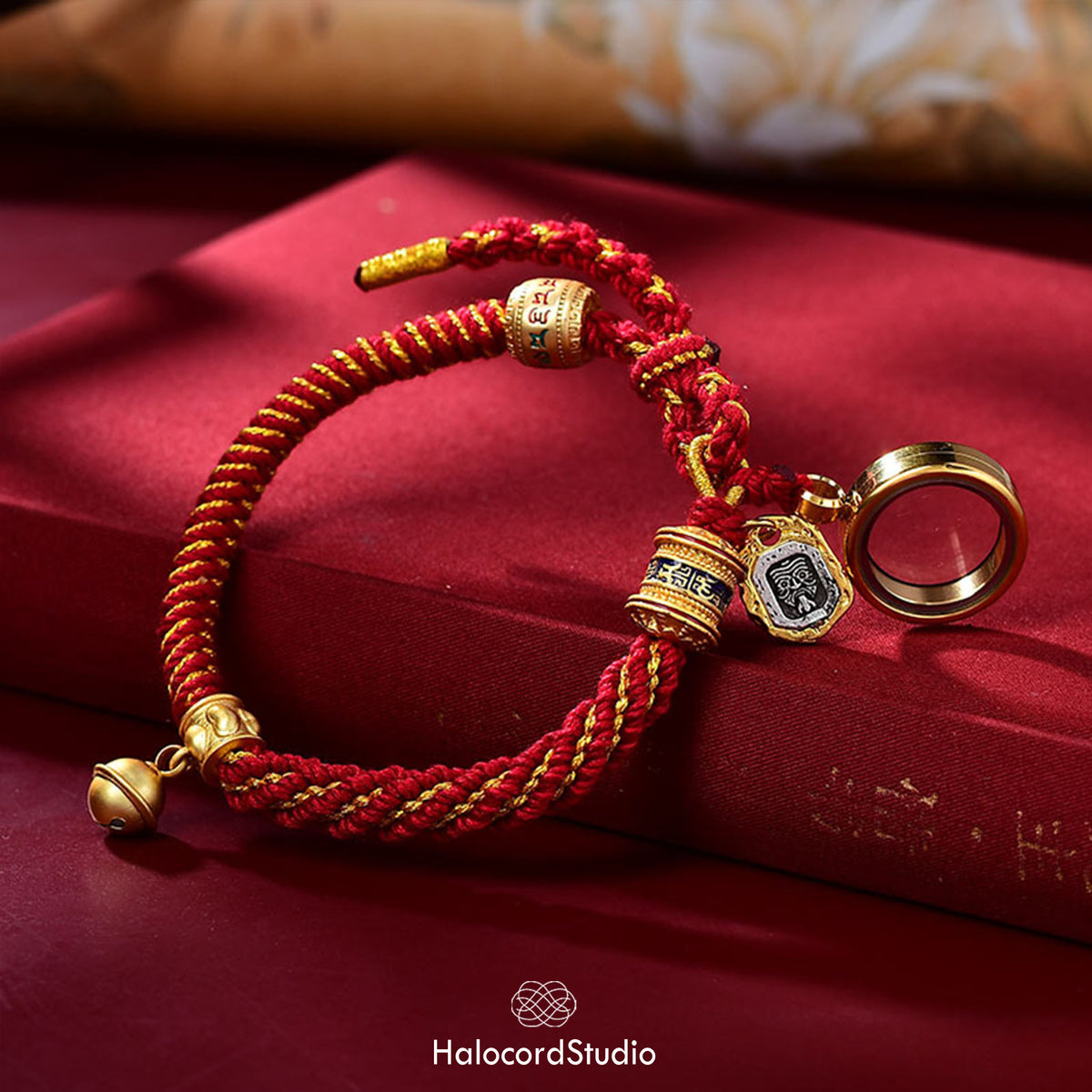 Red handwoven Tibetan lucky knot bracelet with its brass gau amulet box open, displayed on red silk