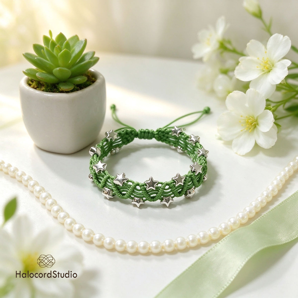 Sage green handwoven star charm bracelet with adjustable sliding knot closure next to a potted succulent