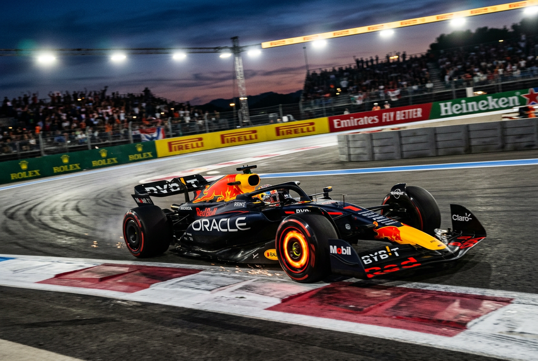 A modern Formula 1 race car roaring through a high-speed apex on a dusk circuit under intense floodlights