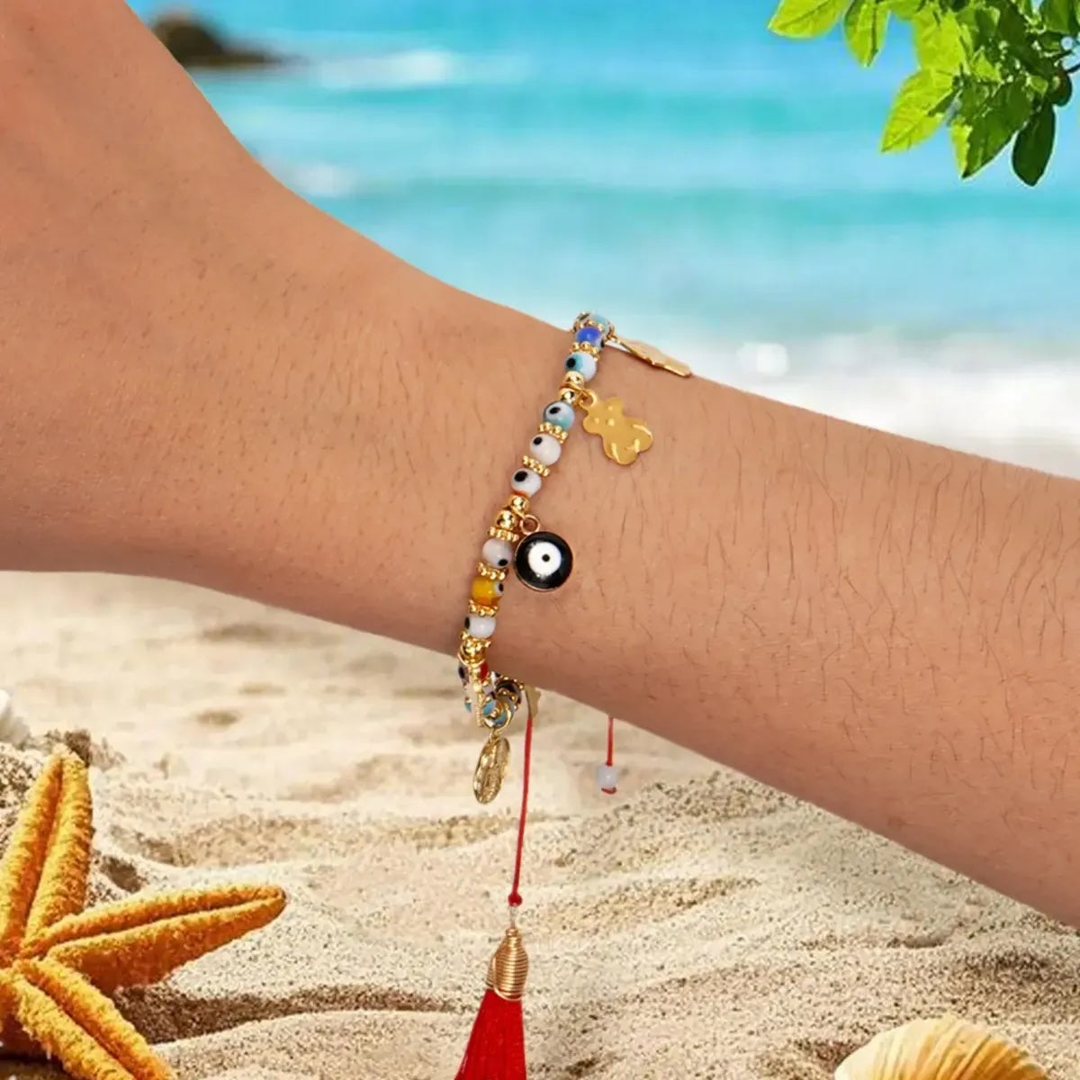 Wrist close-up of adjustable evil eye red string bracelet with sliding knot and red tassel against beach sand