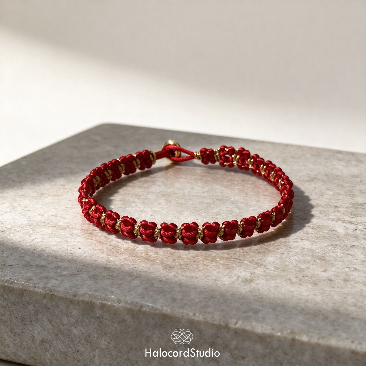 Close-up of the finished red string bowknot bracelet with gold metallic accents and button closure on stone display