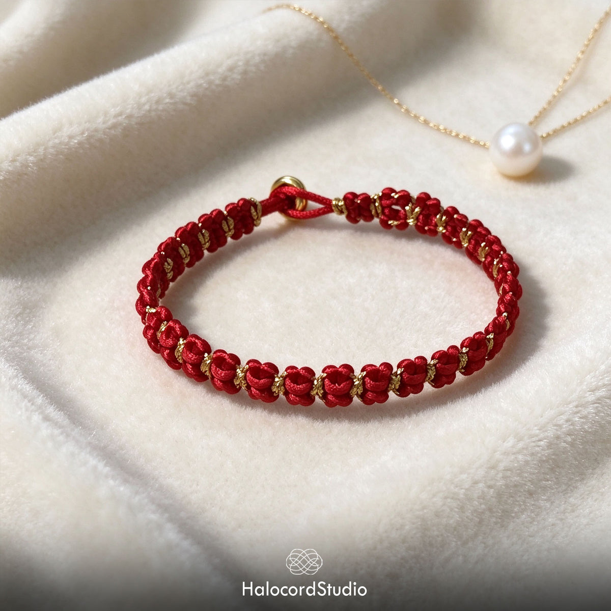 Finished red and gold bowknot braided bracelet displayed on soft white velvet beside a pearl necklace