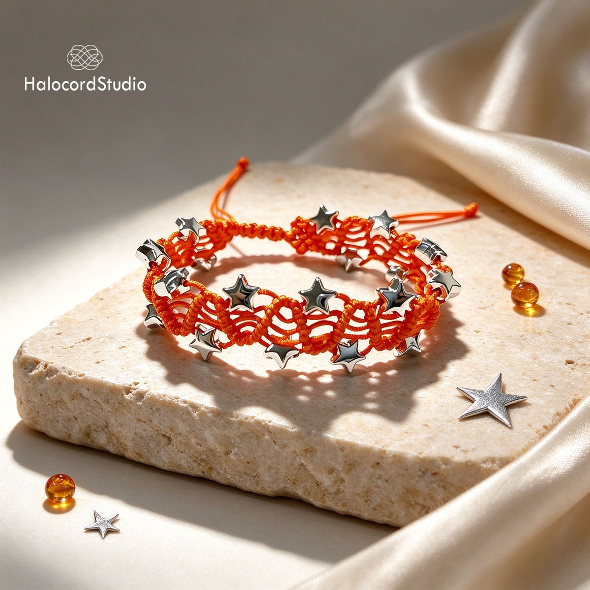 Sunset orange star charm macrame bracelet with silver stars on a limestone display pedestal